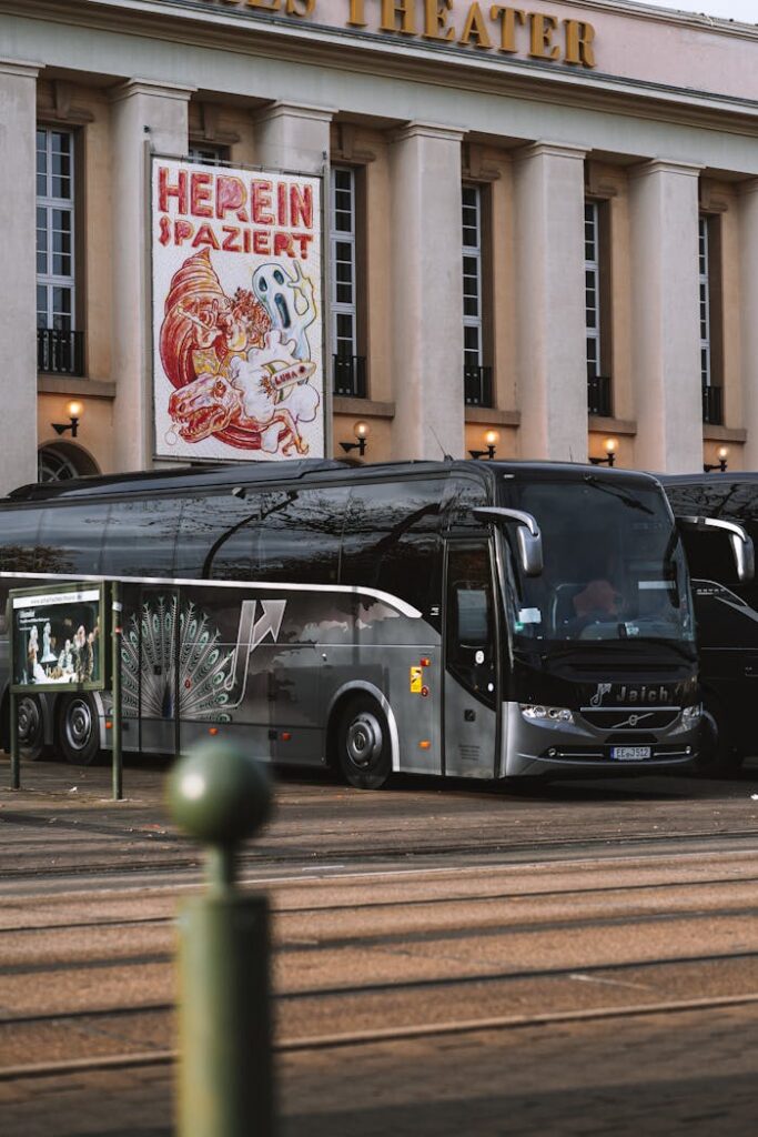 A modern travel bus parked outside a historic theater with classic architecture.